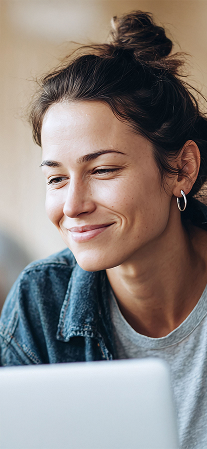 Junge Frau mit braunen Haaren schaut lächelnd auf ein Laptopdisplay