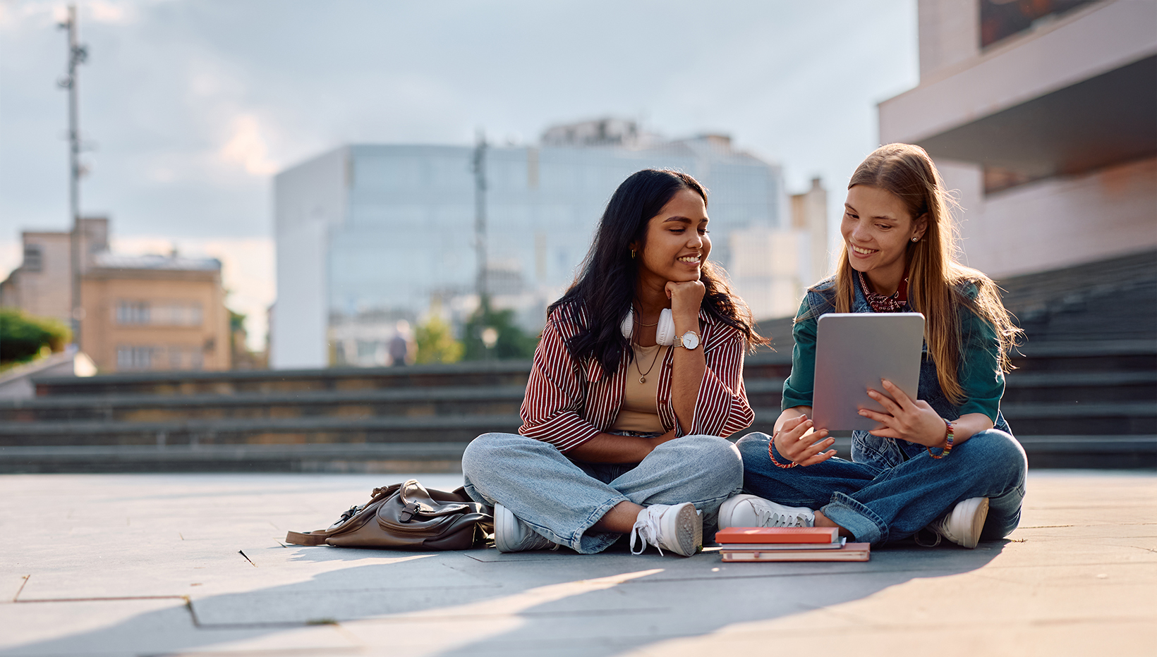 Zwei junge Frauen sitzen auf dem Boden draußen auf dem Boden und schauen gemeinsam in ein Tablet