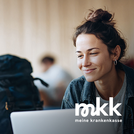 Junge Frau mit braunen Haaren schaut lächelnd auf ein Laptopdisplay