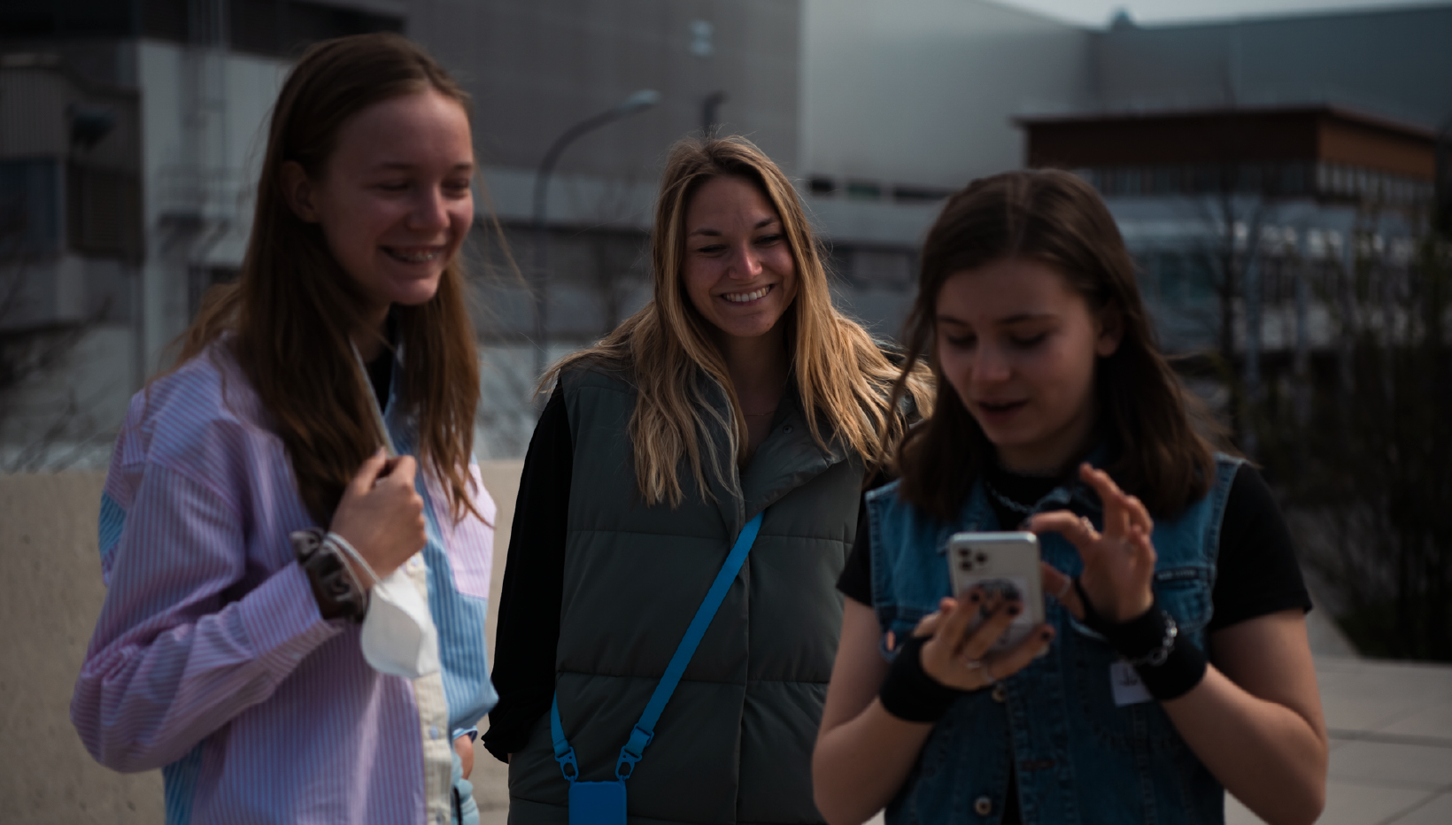Drei lächelnde junge Frauen sehen auf ein Smartphone