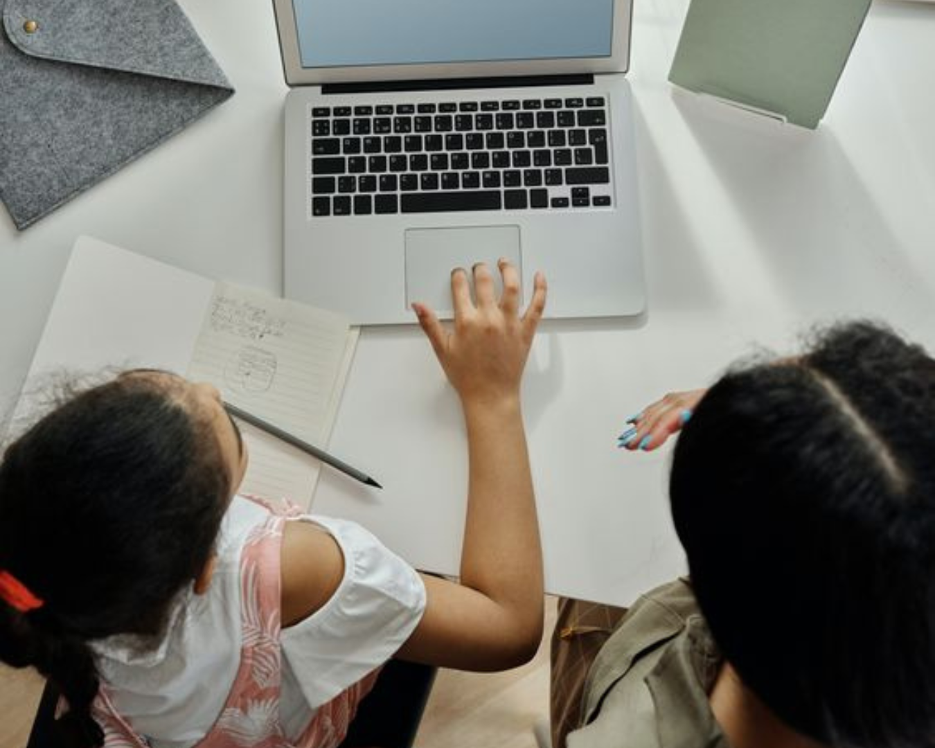 Un niño trabaja en un ordenador portátil con un adulto, tomando notas en un cuaderno y, posiblemente, participando en actividades de aprendizaje o investigación en línea. El entorno fomenta la colaboración y la educación.