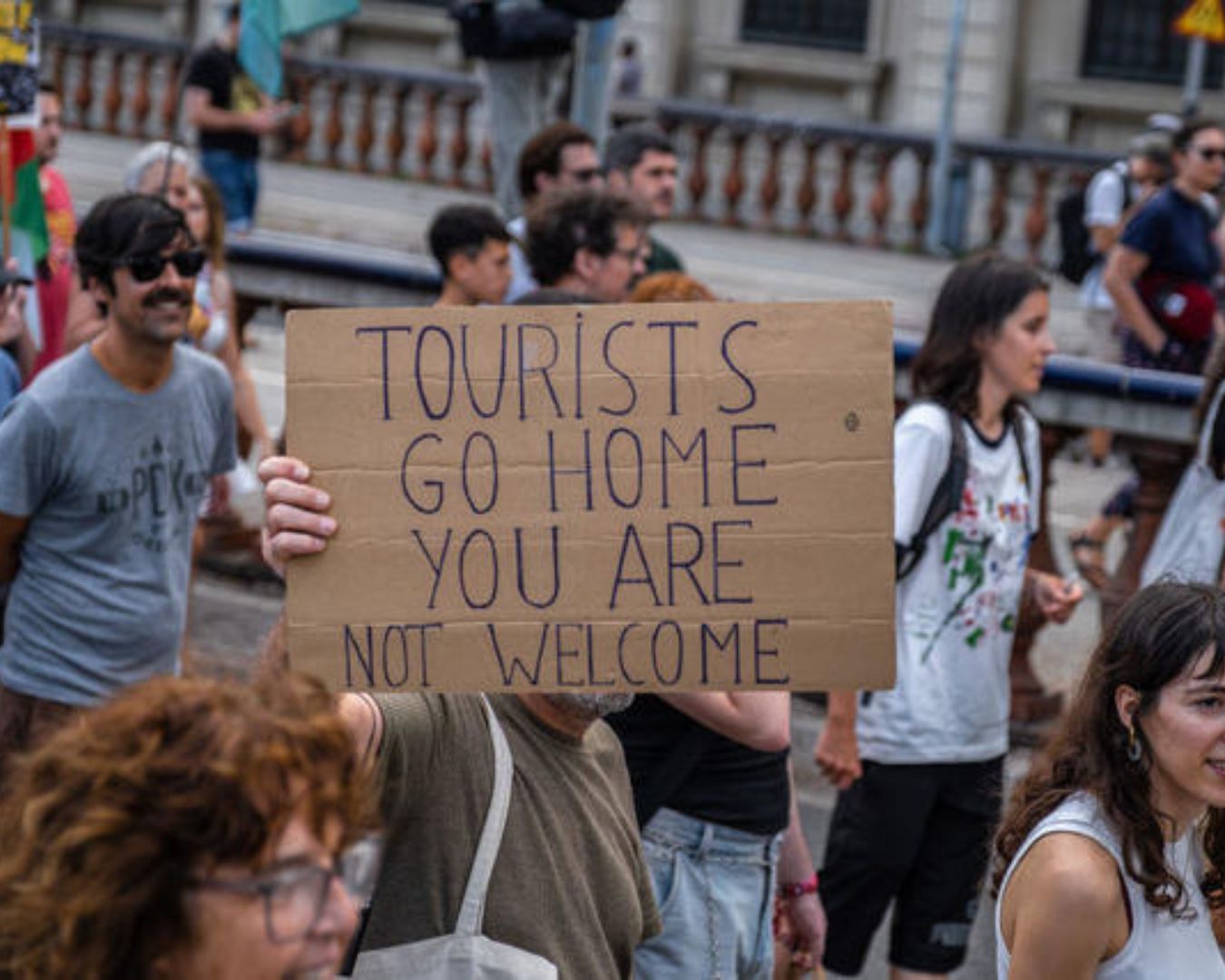 Una persona sostiene un cartel de cartón en el que se lee: «Turistas, iros a casa, no sois bienvenidos», durante una protesta, muestra de la frustración local con el turismo.