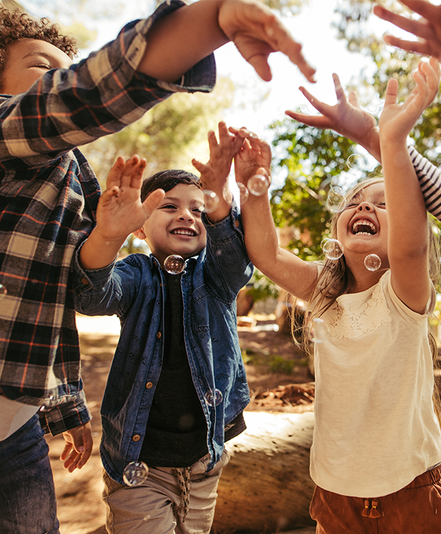  Un grupo de niños ríen y juegan al aire libre, alcanzando alegremente las burbujas en el aire. La escena capta la emoción y la energía despreocupada de la diversión infantil en la naturaleza.