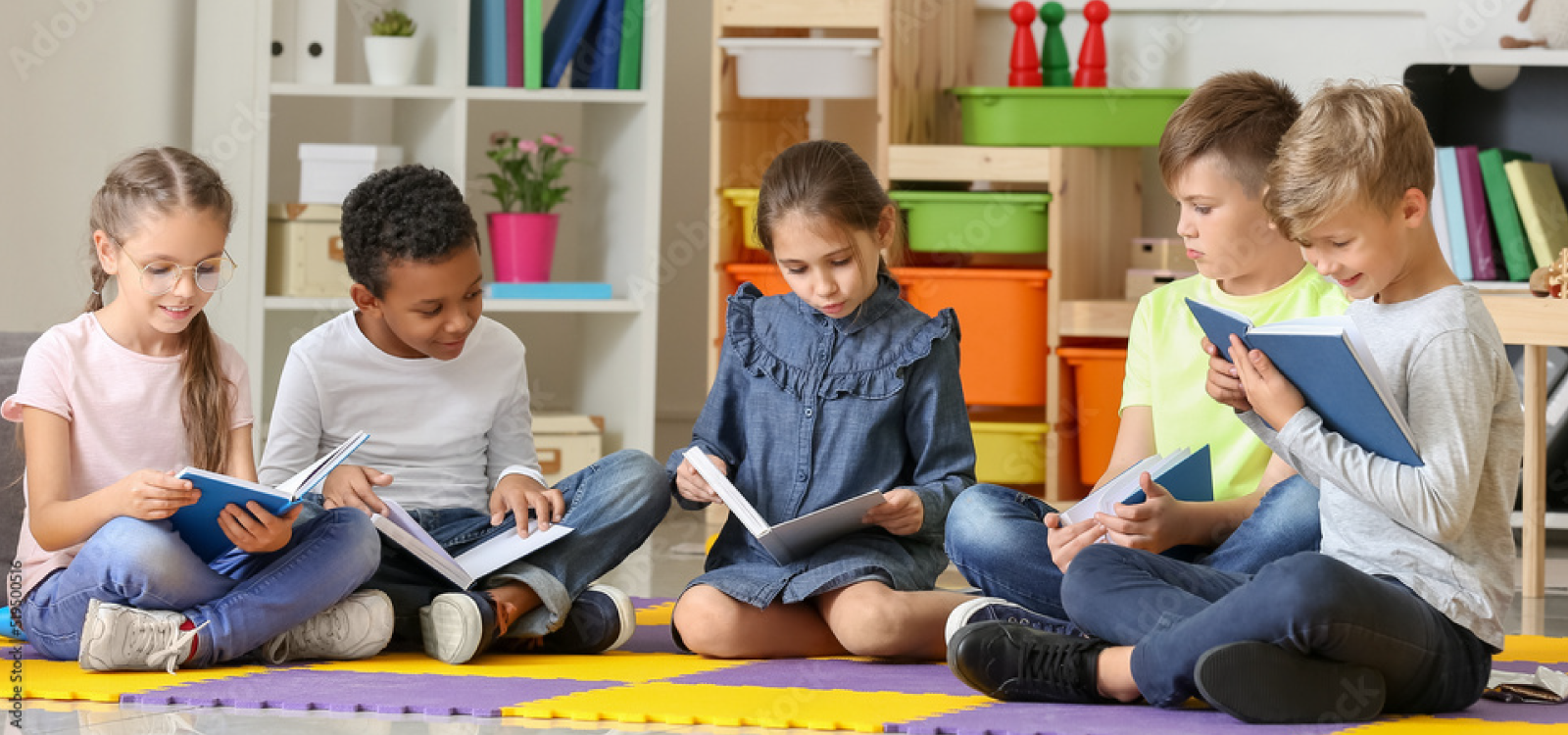 A group of toddlers are sitting on the floor, all holding a book and reading it together.