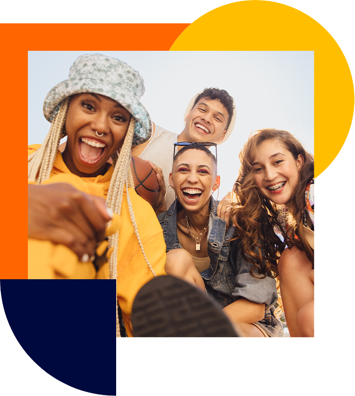 Three women and a man of young age and from different backgrounds look into the camera and all have a smile on their faces.