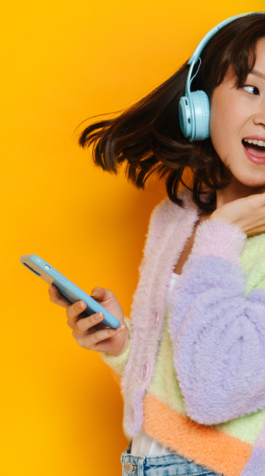 Girl happily listening to an audio book with headphones while holding her mobile phone in her hand. The background is yellow.