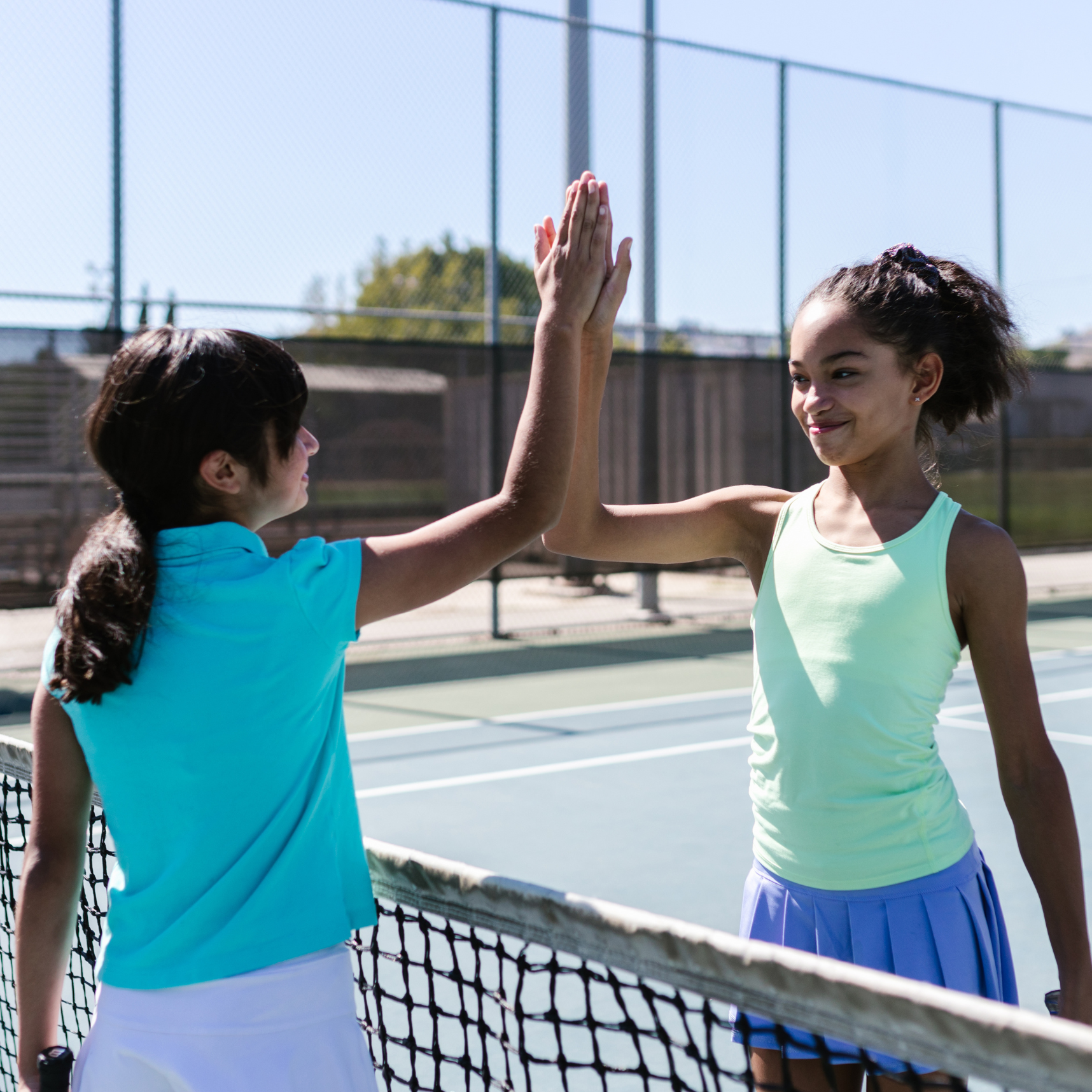 Two girls clap their hands with a smile during a tennis match.