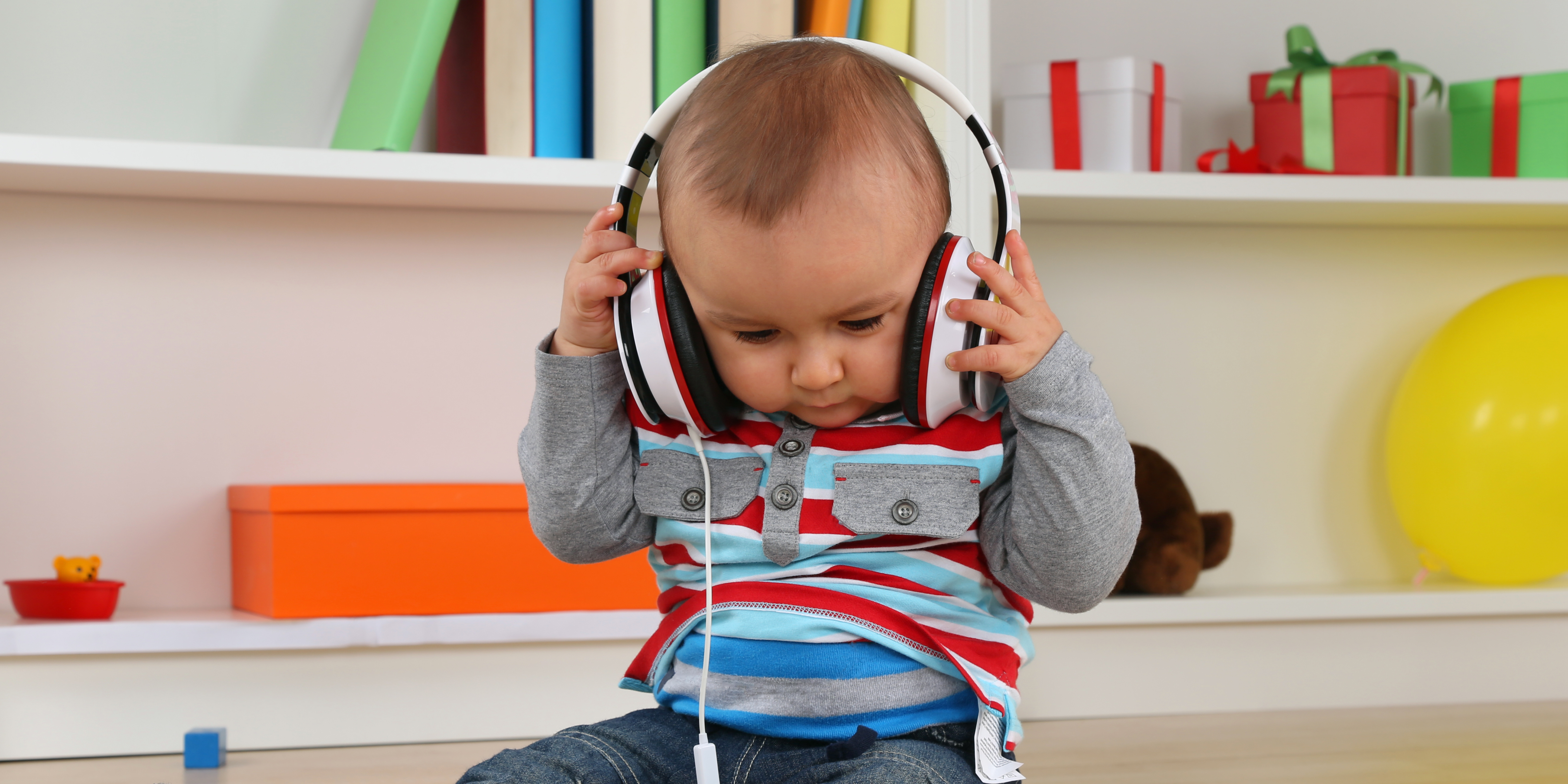 A baby in a child's room has headphones on and is holding them while looking at the floor.