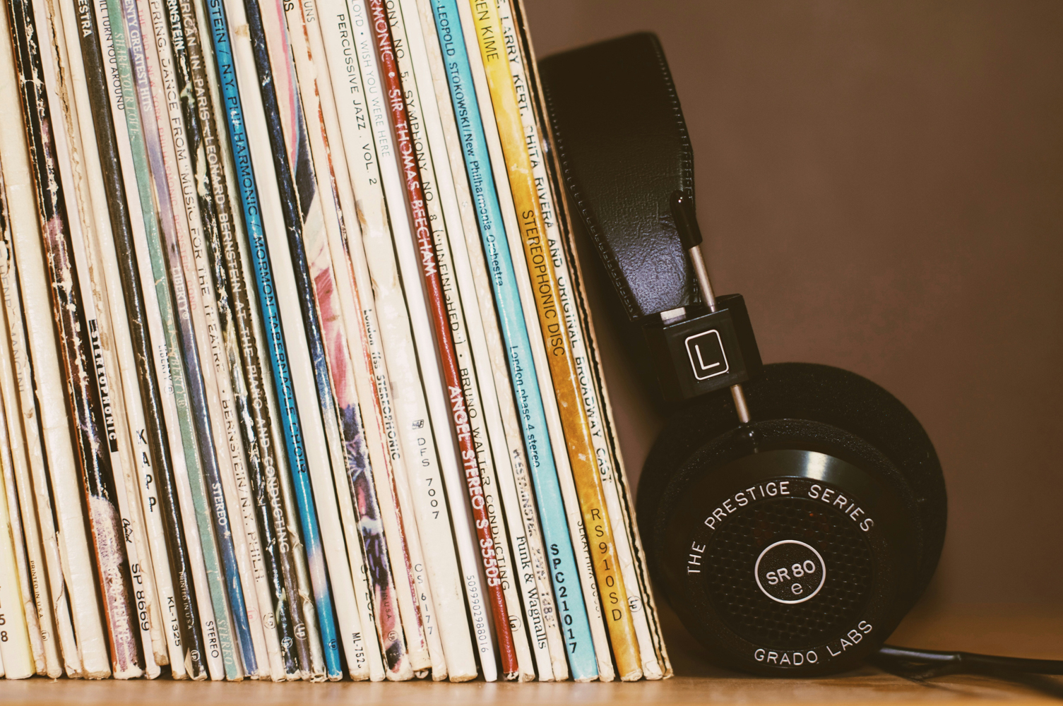 A row of records standing close together on a shelf, with a pair of black headphones leaning next to them.