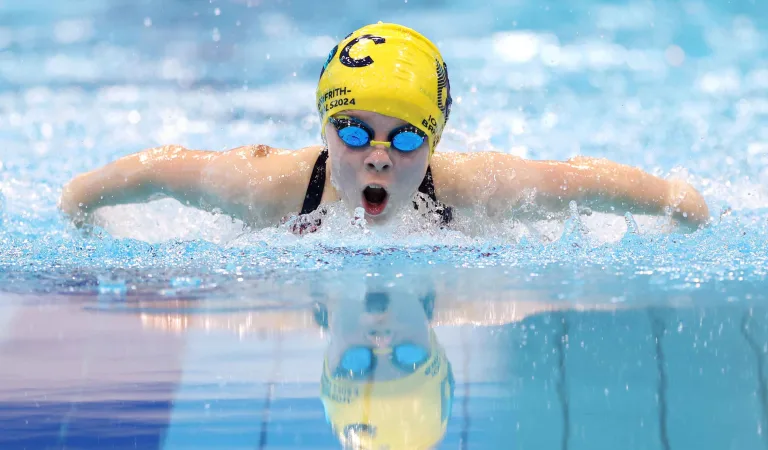  Swimmer in a yellow cap and goggles powers through the water in a butterfly stroke, intense focus reflected on the surface.