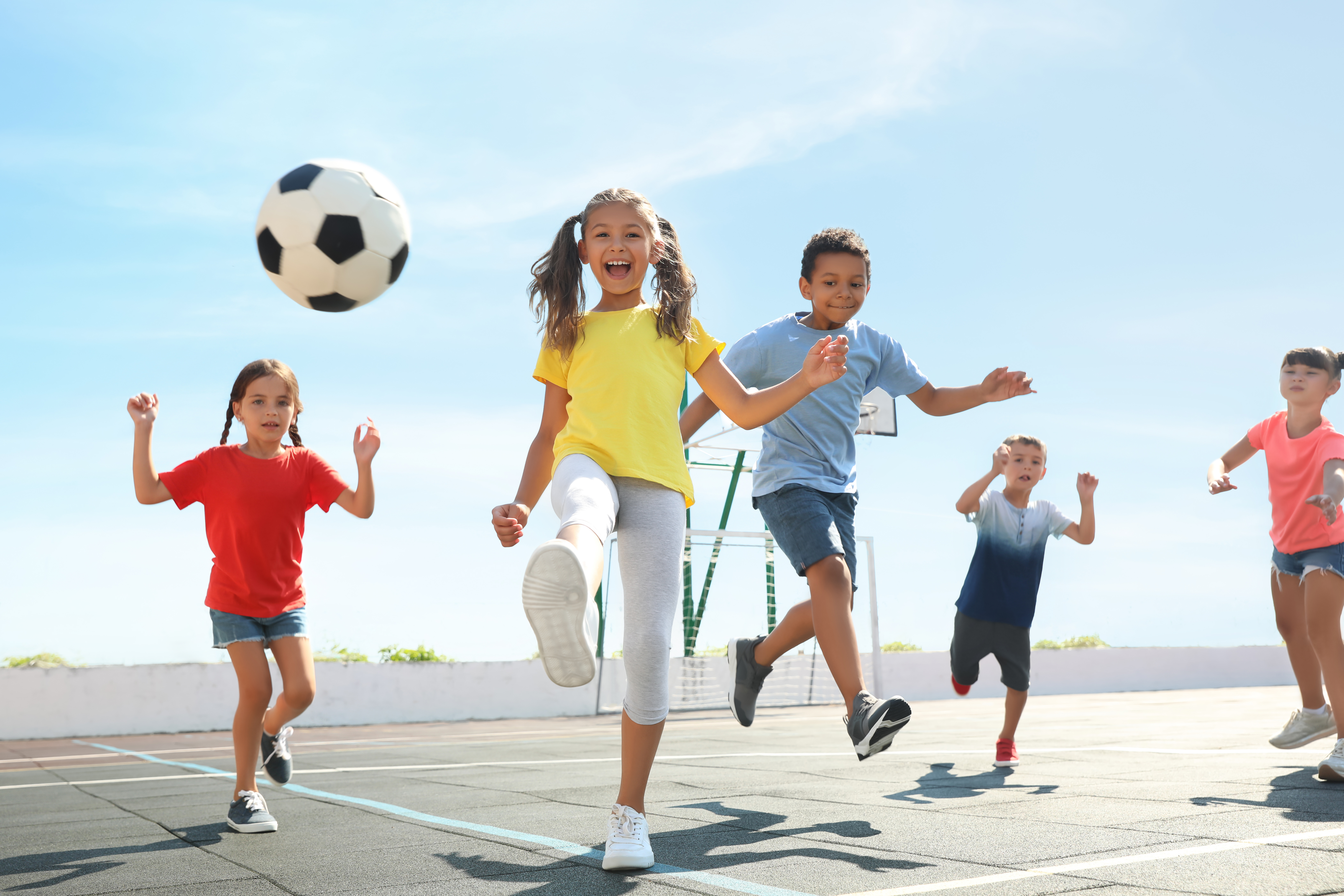 Girls and boys play football happily on an outdoor pitch.