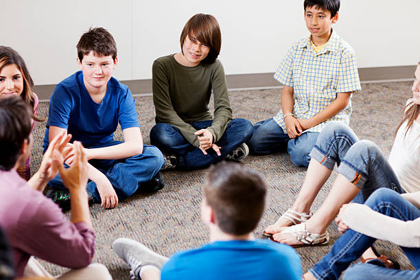 A group of young people sit in a circle and talk to each other. Everyone is listening carefully.