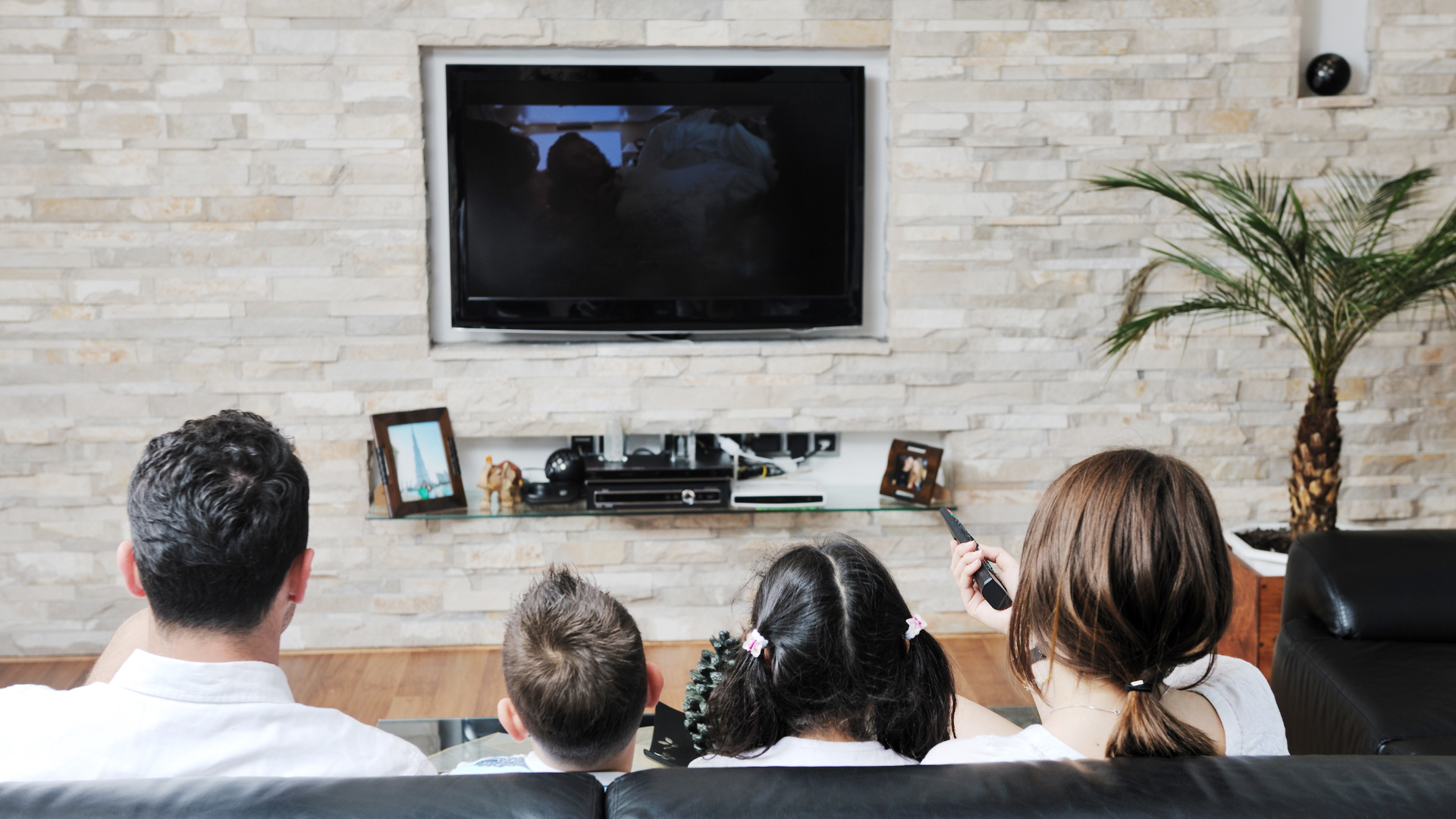 A family is sitting on the couch in the living room watching TV.