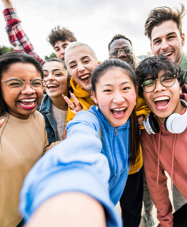 A diverse group of happy young people takes a cheerful selfie together, all smiling and radiating joy and friendship.