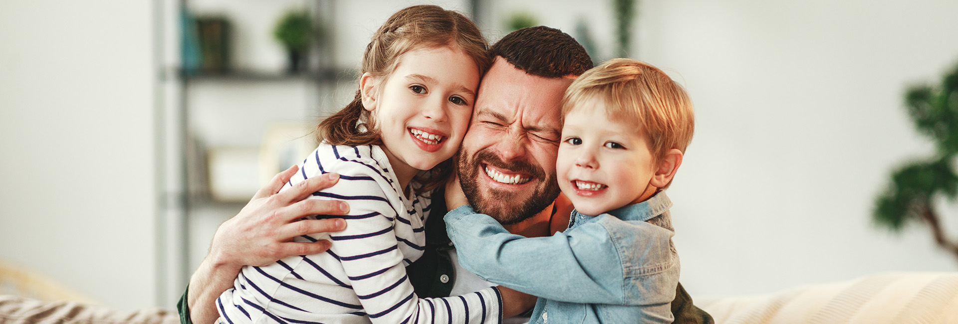 A father hugs his two smiling children, a girl and a boy. All three appear happy, showing a close bond.