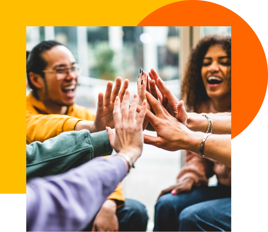 A group of adults sit in a circle in the office and all put their hands together in the middle.